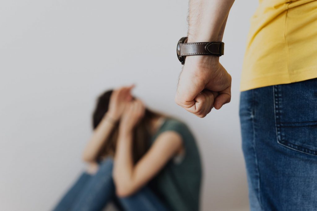 Man Clenching Fist Near a Woman Covering Face While Sitting