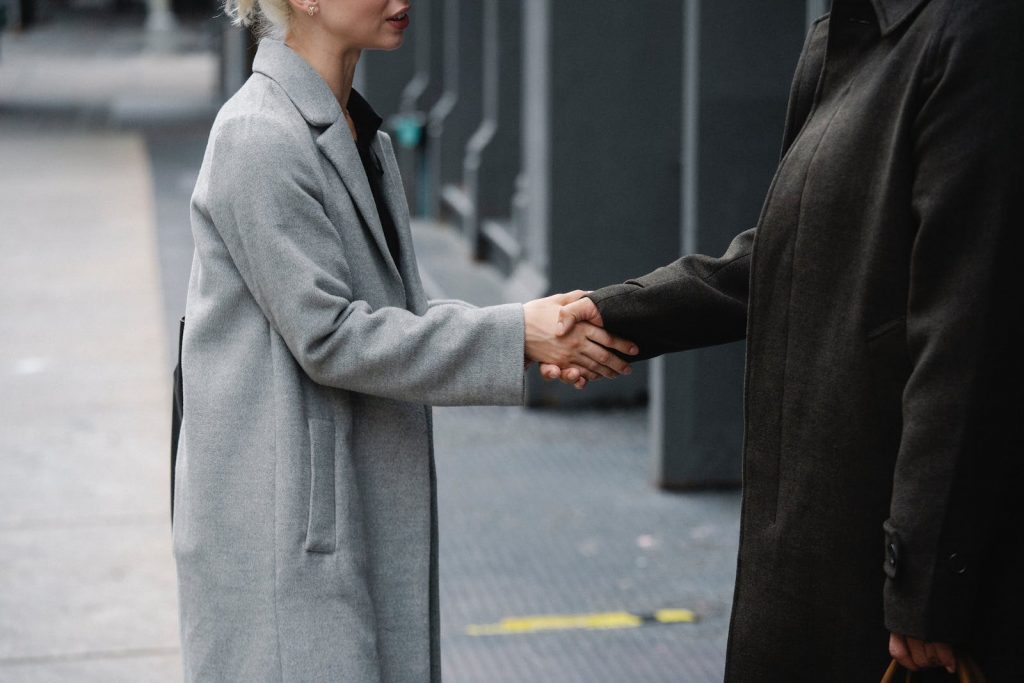 Crop anonymous man and woman in elegant coats shaking hands on street while having meeting in city downtown