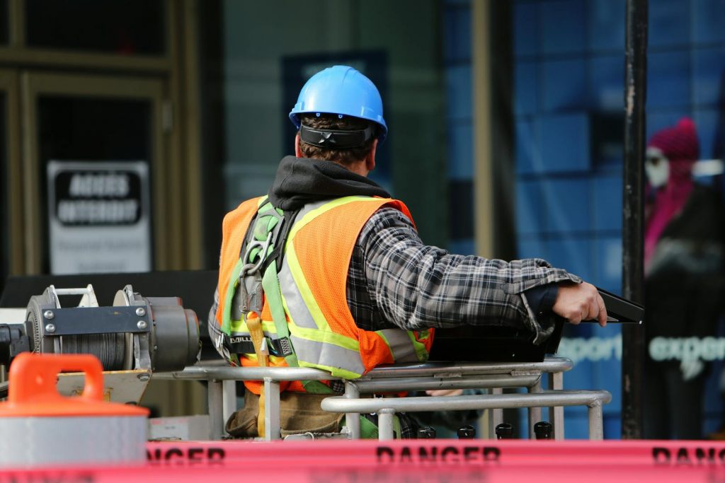 Photo by Life Of Pix A construction worker wearing a blue helmet and safety vest operates equipment at an urban construction site.